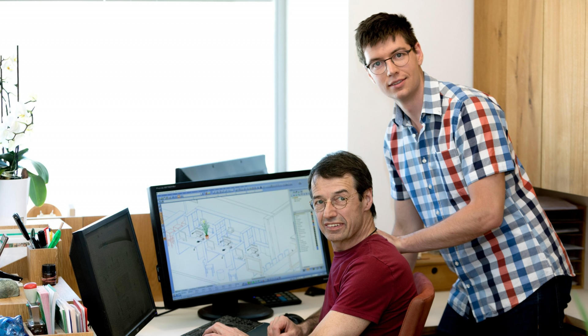 Tischlermeister Max Schlemaier und Sohn und Geschäftsführer Markus gemeinsam in einem Büro während sie an einem Computer arbeiten. 